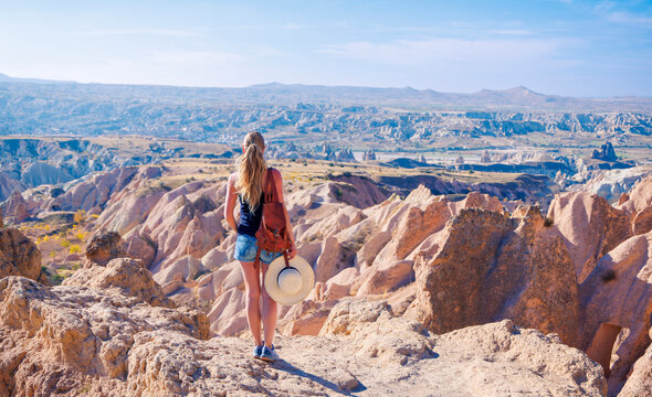 Young woman with backpack looking at the breathtaking landscape of Cappadocia, authentic travel adventure and freedom concept in Turkey