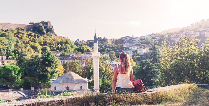 Young female tourist looking at the historic old town of Berat and mosque minaret, authentic travel adventure and cultural heritage concept in Albania