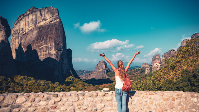 Joyful female tourist raising arms in front of the spectacular Meteora rock pillars, authentic travel freedom and spiritual journey concept in Greece