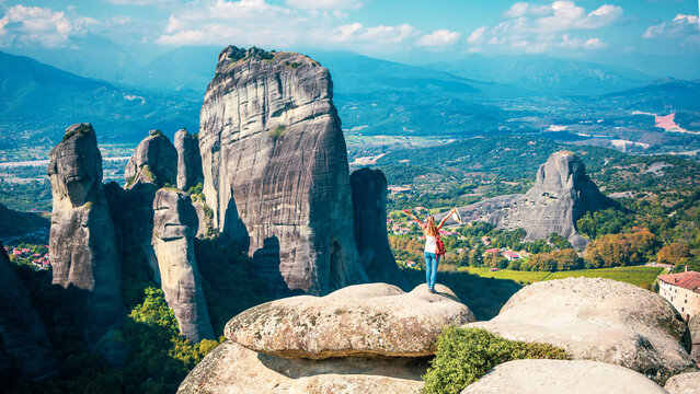 Young female hiker standing on a high cliff overlooking the majestic Meteora rock valley, authentic travel achievement and breathtaking freedom concept in Greece