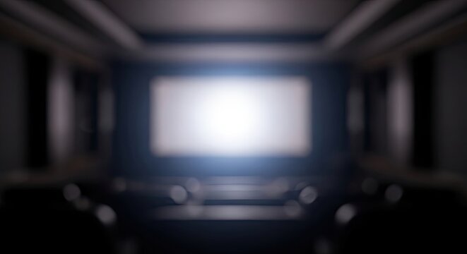 Empty dark movie theater with blurry glowing white screen and seats.