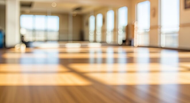 Blurred background of an empty sunlit room with a polished wooden floor and large windows.