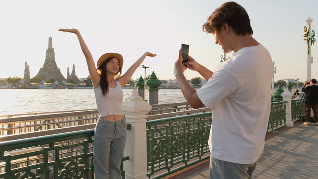 Young Couple Taking Photos by Chao Phraya River with Wat Arun Background