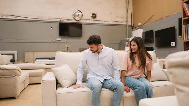 Young couple choosing and testing a sofa in a furniture store showroom