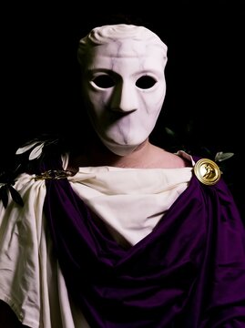A man wearing an ancient Greek marble-white theatrical tragedy mask with hollow eyes
