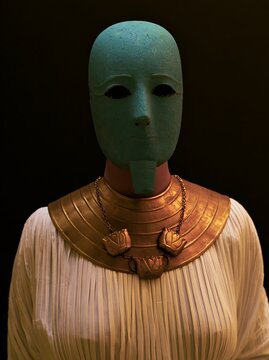 A woman wearing an ancient Egyptian faience turquoise mask with kohl-lined almond eyes