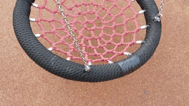 Close up view of a circular rope nest swing hanging still in an outdoor play area.