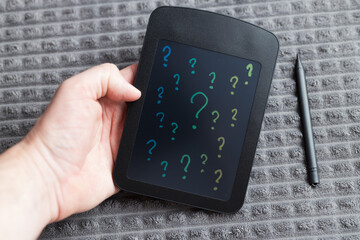 Handheld electronic writing tablet with stylus showing colorful question marks for brainstorming and idea prompts on fabric surface © Andrii Zastrozhnov