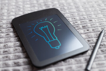 Electronic writing tablet with glowing lightbulb drawing on black screen for idea background and brainstorming wallpaper © Andrii Zastrozhnov