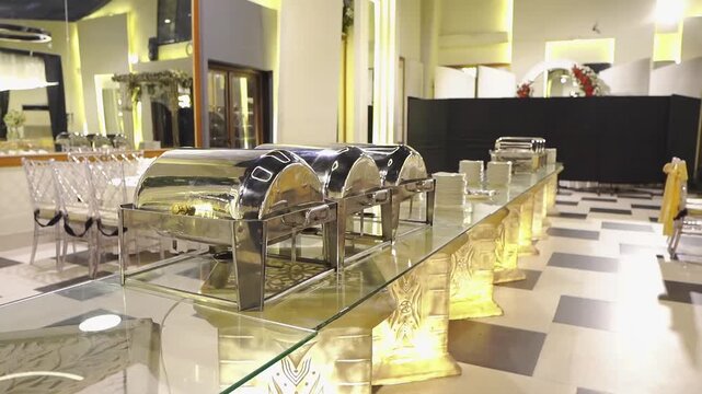 Elegant wedding buffet setup featuring stainless steel chafing dishes, serving stations, and modern banquet hall decor. Beautifully arranged catering area prepared for guests at a wedding reception, c