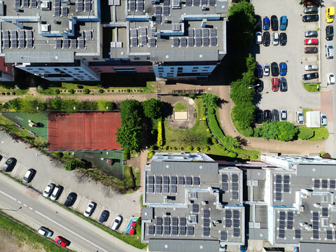Top-down aerial view of modern apartment buildings with solar panels on roofs and a sports court, sustainable housing concept.