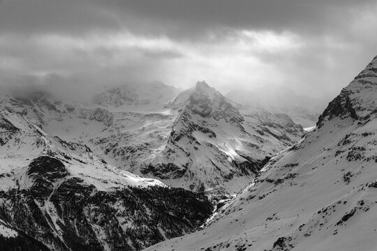 Dark clouds and wafts of mist surround the snow-covered summit of Mount Le Besso, view from the Sorebois summit station, black and white photo, Val d'Anniviers, Valais Alps, Canton Valais, Switzerland