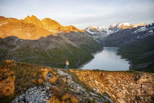 Mountaineer on the summit of Mont de la Blana, alpenglow at sunset, view of a blue mountain lake, Lac des Dix reservoir, behind mountain peak Mont Blanc de Cheilon with glacier, H&eacute;rm&eacute;nence, Valais Alps, Valais, Switzerland