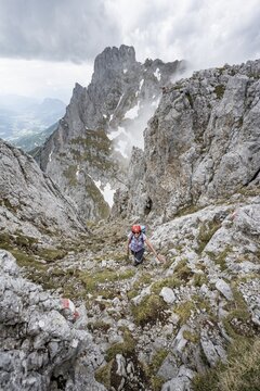 Mountaineer with helmet on a narrow hiking trail, ascent to the Maukspitze, clouds moving around the mountains, Ackerlpitze in the background, Wilder Kaiser, Kaiser Mountains, Tyrol, Austria