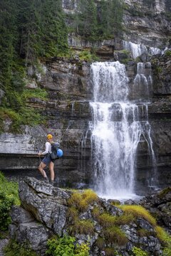 Young pretty hiker standing on rocks in front of Cascata di Mezzo waterfall, long exposure, Vallesinella, Brenta, Trentino, Italy