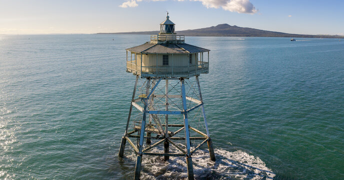 Auckland's Rangitoto Island is visible in the distance from the historic Bean Rock Lighthouse in Waitemata Harbour, New Zealand. The lighthouse guides ships.