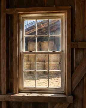 Rustic barn double hung window showcasing scenic view of golden agriculture hay bales outside farm.