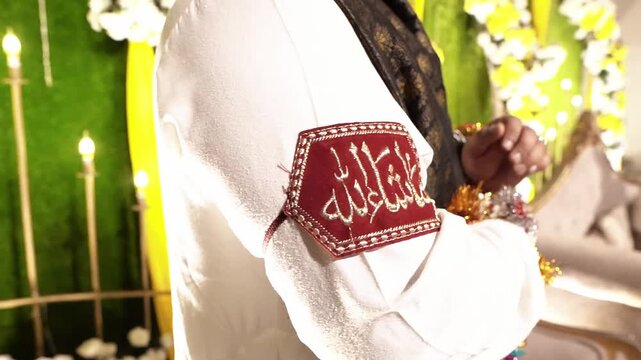 Close-up shot of an Asian Muslim groom wearing a traditional red wedding arm band featuring beautiful "Mashallah" embroidery during a wedding ceremony. celebration in South Asian Muslim weddings. 