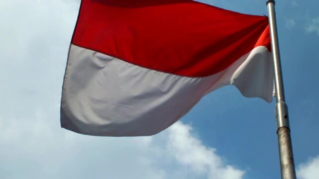 Indonesia national flag waving in the wind with clear blue sky background. Nation patriotsm. The Hari Kemerdekaan Indonesia. Independence day of The Republic of Indonesia.
