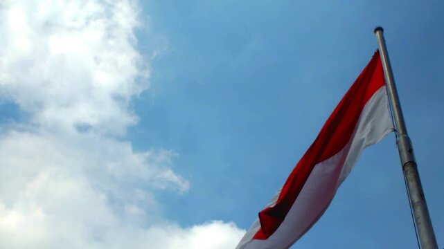 Indonesia national flag waving in the wind with clear blue sky background. Nation patriotsm. The Hari Kemerdekaan Indonesia. Independence day of The Republic of Indonesia.