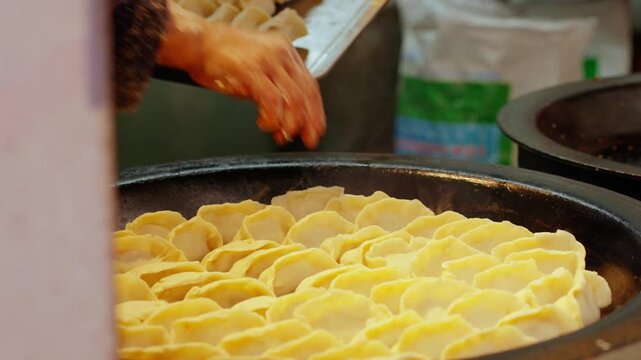 Cook prepares fresh dumplings in a large pan at a food market, hand placing dough filled pieces