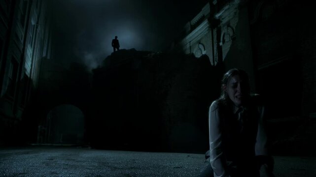 Distressed woman kneeling in dark alley while a shadowy figure watches from the distance