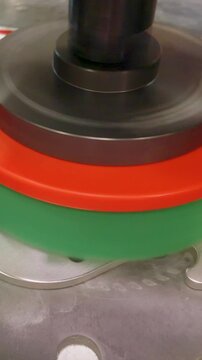 Deburring and linishing machine polishes a sheet metal part with a rotating abrasive wheel, removing burrs and refining edges on an industrial workbench in a workshop. Vertical format.