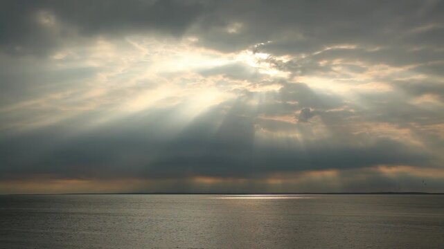 Majestic sunbeams pierce through heavy clouds to illuminate the quiet surface of the sea