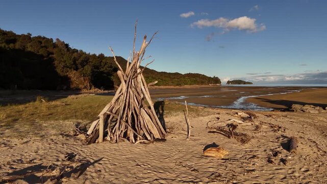 Scenic view of a driftwood teepee structure on Marahau Beach at the Abel Tasman National Park in New Zealand.