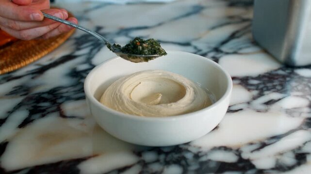Close up view of a creamy white hummus or pur&eacute;ed dip swirled elegantly inside a small ceramic appetizer bowl on a dark textured marble countertop backdrop, gourmet finger food styling.