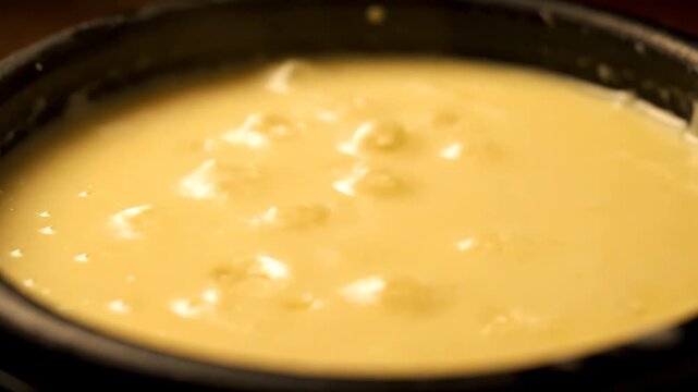 Close-up view of rich, creamy melted cheese or traditional fondue bubbling softly in a dark pot ready for dipping