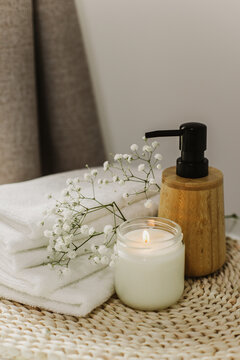 Minimalist still life of luxury spa essentials. White cotton towels with visible textured, bottle with oil and soy wax candle.