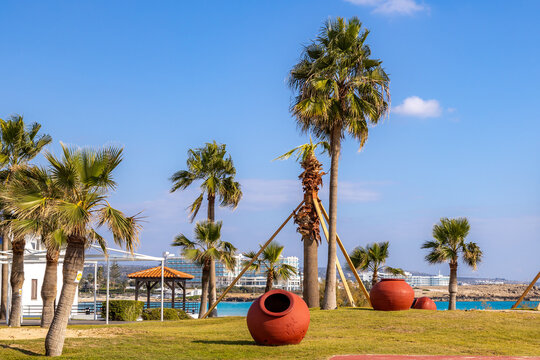 Decorative clay amphora pots on green grass lawn of resort park near sea. Beautiful tropical garden view with palm trees during winter low season, Nissi Beach, Ayia Napa, Cyprus.