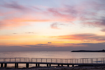 Obraz premium Peaceful and calm mediterranean sea under beautiful pastel pink sunset sky in winter low season. Quiet twilight marine landscape with pedestrian walking promenade walkway, Ayia Napa, Cyprus