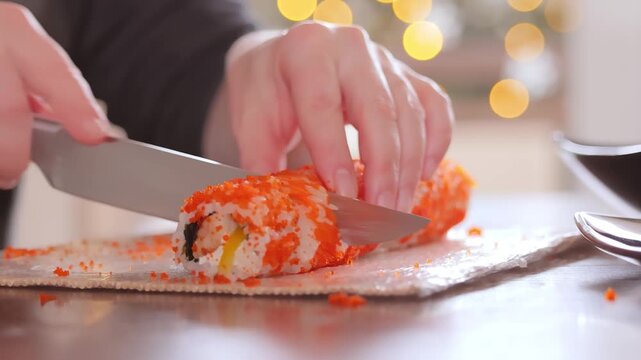 Professional chef slicing fresh california sushi roll with sharp knife on wooden board in kitchen.