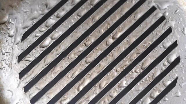 Ultra HD 4K macro video featuring a circular metal grill pattern covered with water droplets. 4K Abstract Metal Grill with Water Droplets &ndash; Industrial Texture Macro Video