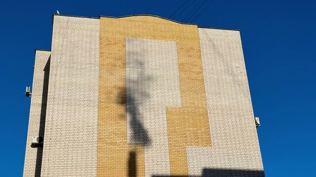 Shadow gas pipe smoke on brick facade under clear blue sky, sunlight casts dark silhouette and elongated pipe shadow