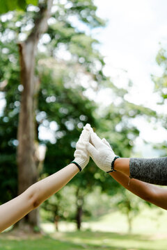 Two people in white work gloves high-five against a soft green background, celebrating successful teamwork and community gardening after outdoor volunteering and shared effort