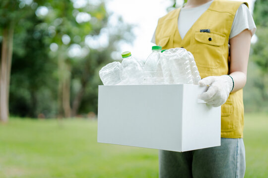 Person wearing gloves and yellow vest holding a box full of plastic bottles for recycling, symbolizing environmental conservation and waste management efforts outdoors
