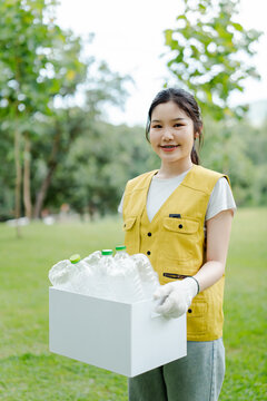 Young woman collecting plastic waste for recycling, actively participating in an outdoor clean-up event for environmental conservation and sustainability in a green park