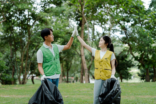 Diverse volunteers celebrating successful park cleanup, high-fiving after collecting trash in garbage bags, promoting environmentalism and sustainable community initiatives