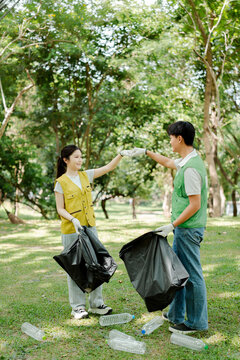 Young volunteers in vests and gloves picking up discarded plastic bottles and rubbish into black garbage bags, actively contributing to park cleanup and environmental protection