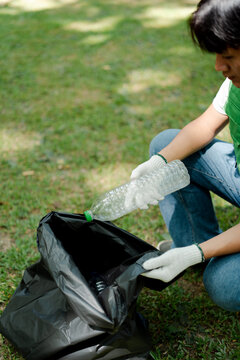Young volunteer wearing gloves and collecting discarded plastic bottles into a trash bag in a park for recycling, contributing to environmental protection and waste management