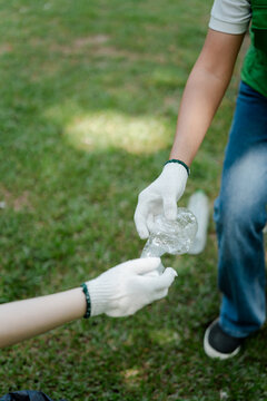 Volunteer hands wearing white protective gloves collecting plastic bottles from the green grass, participating in an outdoor environmental cleanup and recycling activity for sustainability