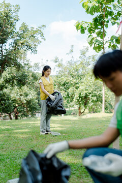 Asian volunteers cleaning up plastic waste and trash in a park, contributing to environmental conservation and sustainability initiatives outdoors