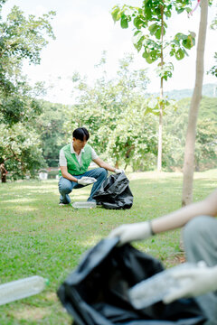 Young man volunteering for environmental cleanup, collecting plastic waste in a park, contributing to nature conservation and sustainability efforts