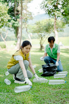 Young asian volunteers clean a sunny park, picking up plastic bottles from the grass and filling trash bags to promote recycling, teamwork and a cleaner, greener future