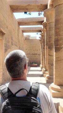Adult male tourist with a backpack walking down a colonnaded corridor in the ancient philae temple, in aswan, egypt