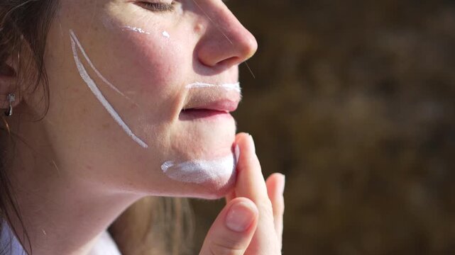 Sunscreen skincare woman applying protective sunblock cream to her face outdoors under bright sunlight during summer vacation to prevent sunburn