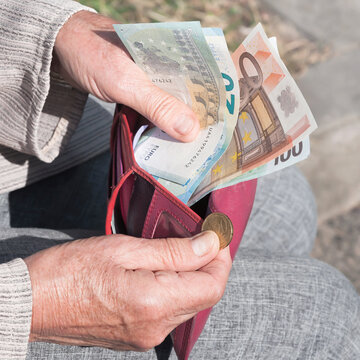 Pink purse, euro banknotes and a coin in the hands of elderly woman.	